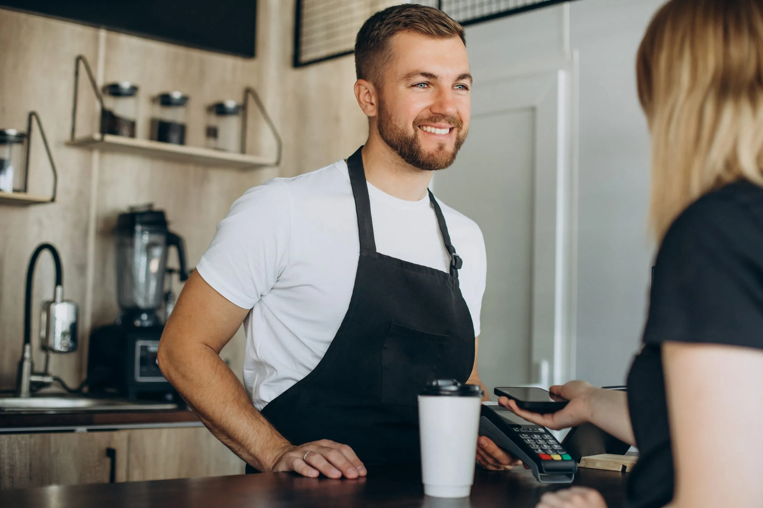 Professionnel du commerce servant une cliente au comptoir avec un terminal de paiement