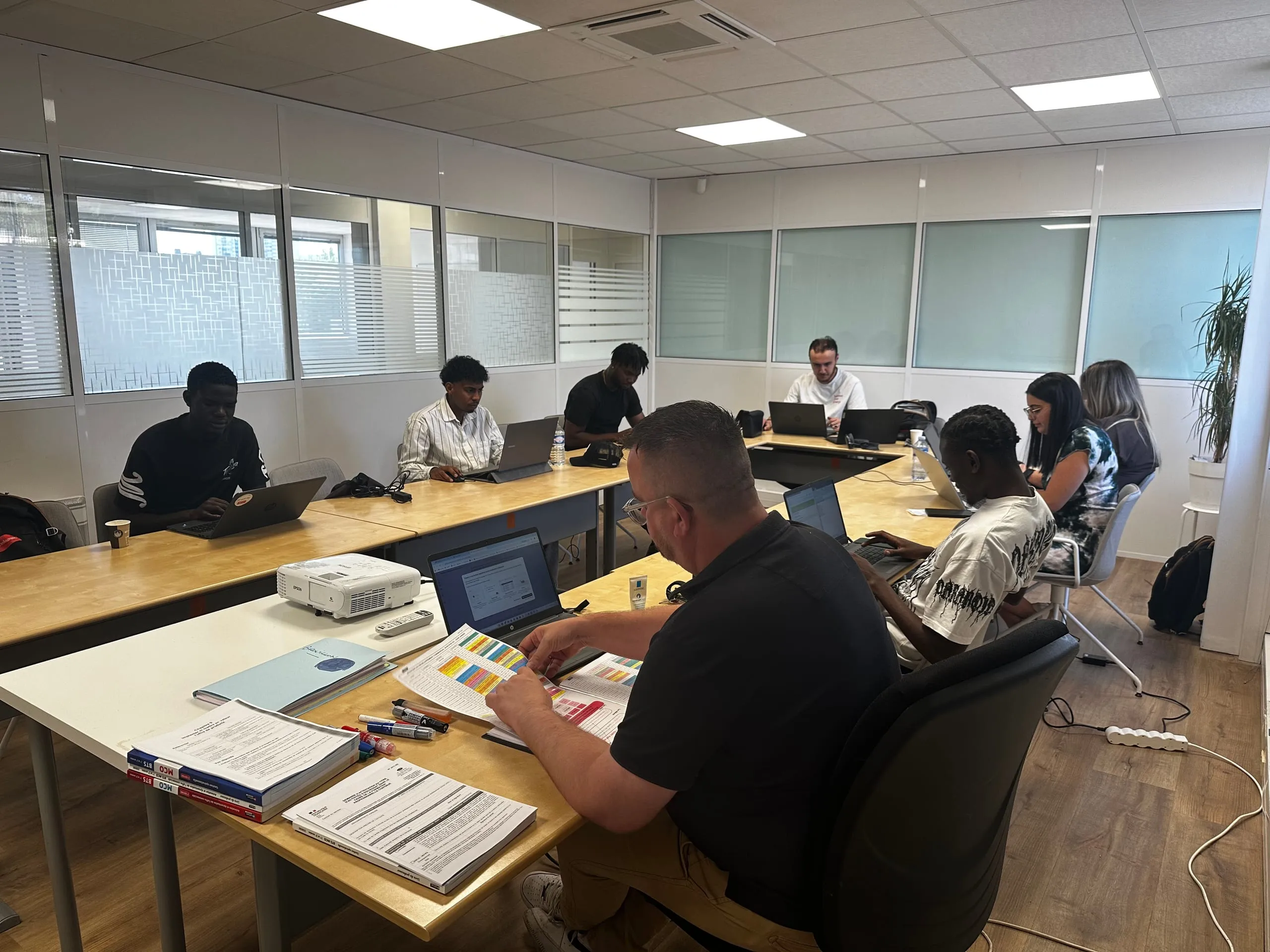 Groupe d’apprenants réunis en salle de formation avec des ordinateurs portables et un vidéoprojecteur.