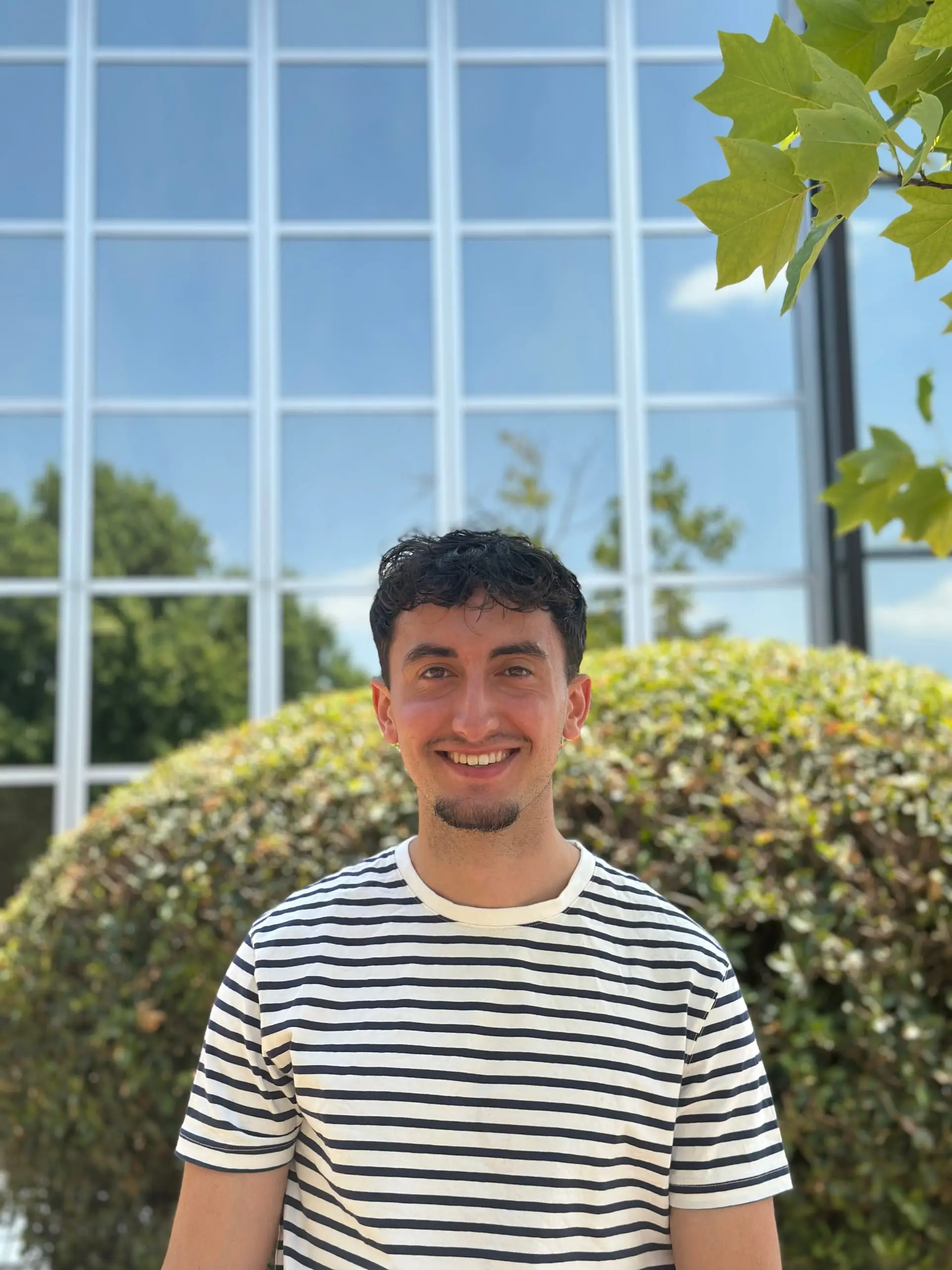 Portrait de Florian Arnaudinaud souriant devant une haie et une façade vitrée.