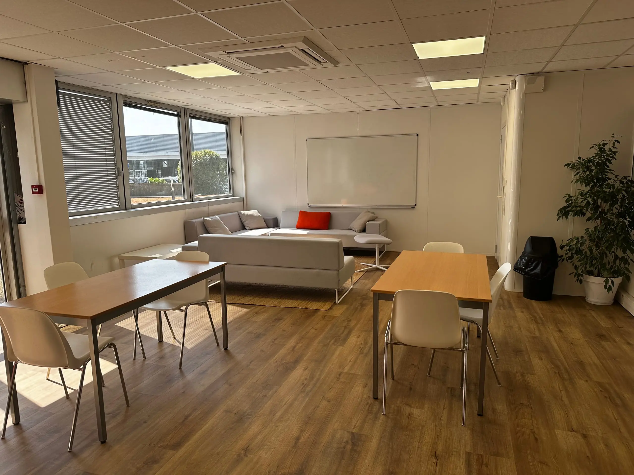 Salle polyvalente du CFA Paedagogia avec tables, canapé et tableau blanc